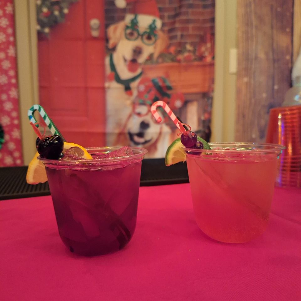 Two colorful cocktails with fruit garnish and candy cane on a red table