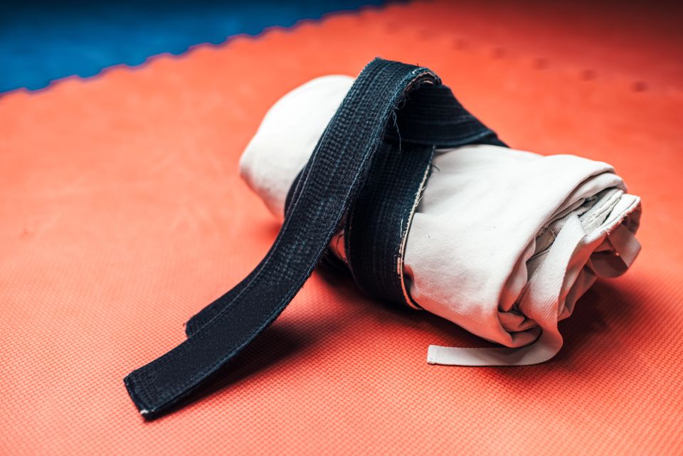 A white karate gi rolled up with a black belt tied around it