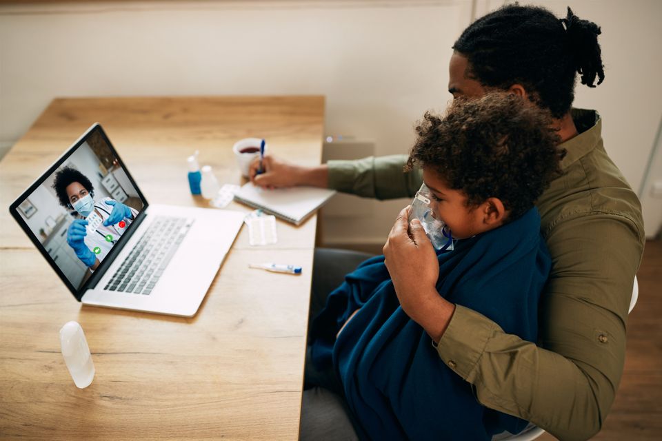 Female doctor talking via video call father who is giving inhaling therapy his son home