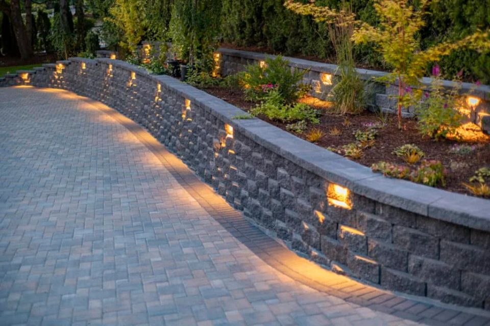 Curved retaining wall with built-in landscape lighting beside a paver driveway at a luxury outdoor living project in Charlotte NC