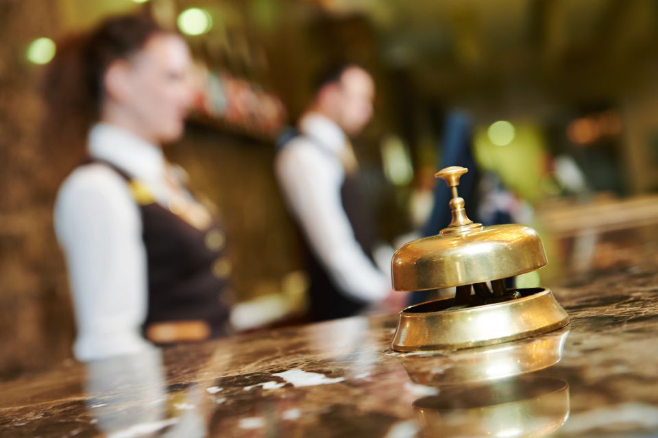 Hotel desk with a golden bell on it with workers in the background behind the desk