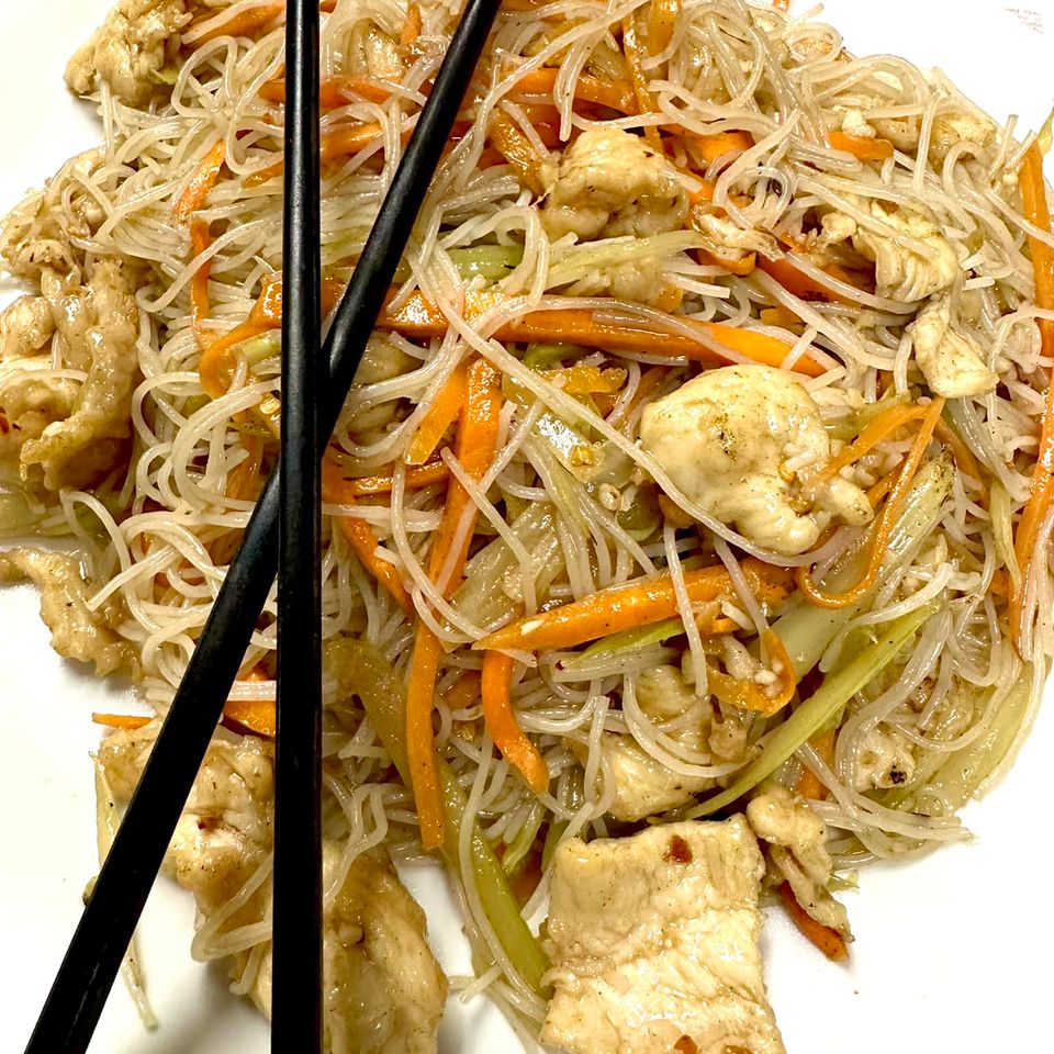 Stir-fried rice noodles with vegetables and protein served on a white plate with black chopsticks.