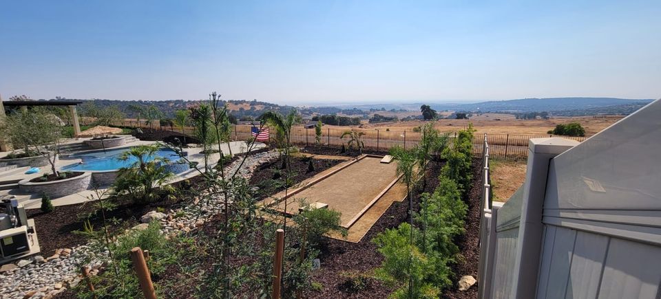 Luxury backyard landscape design in El Dorado Hills featuring a custom bocce ball court, infinity-edge swimming pool, stone retaining walls, and drought-tolerant planting with a panoramic valley view