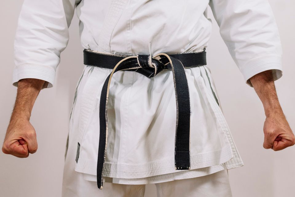 A person who is a black belt with a white gi on with their fists clinched