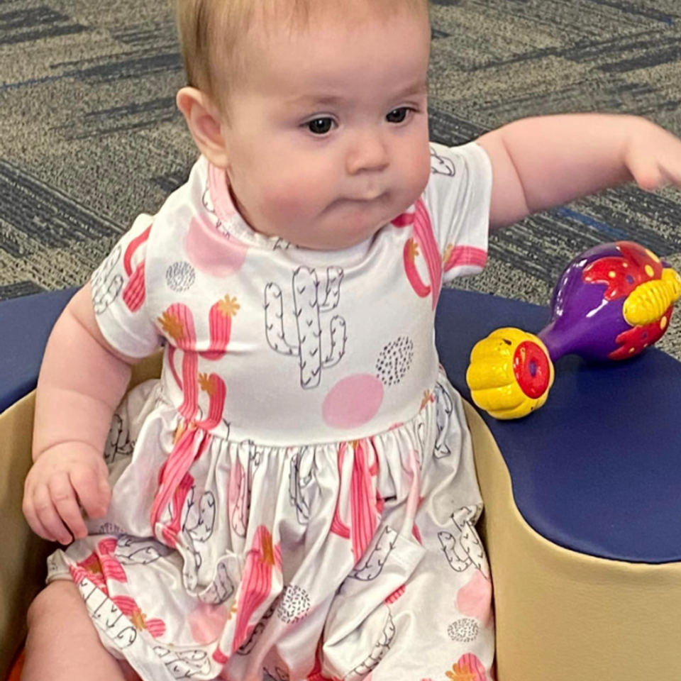 Infant with Down syndrome sitting with colorful toys during a Down Syndrome Association of the Valley early childhood program.