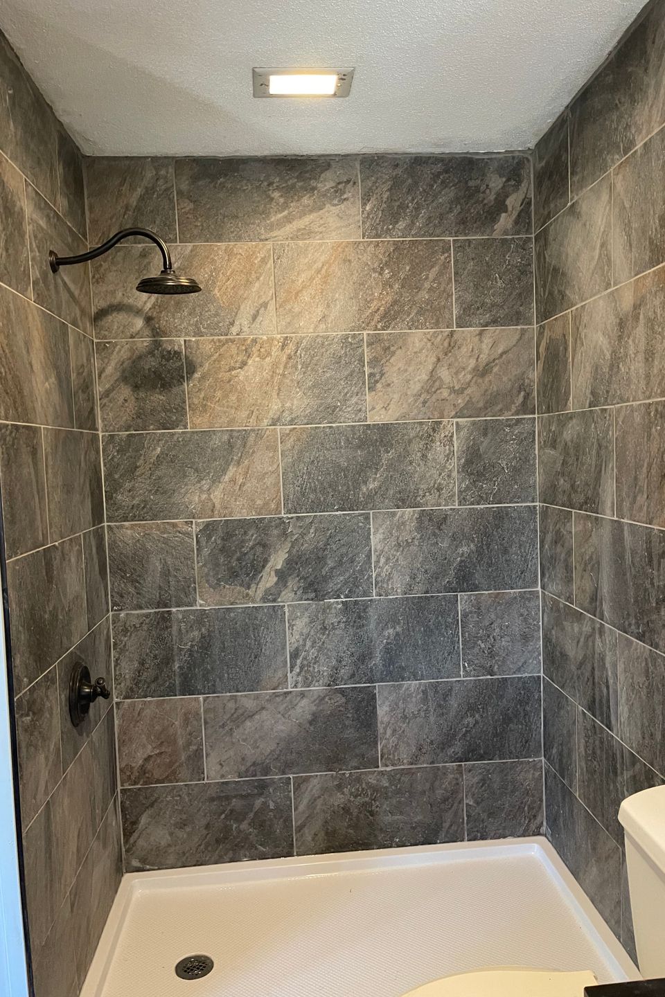 Remodeled walk-in shower featuring large gray tile walls, a white shower base, and black fixtures installed by R.E.P. Companies.