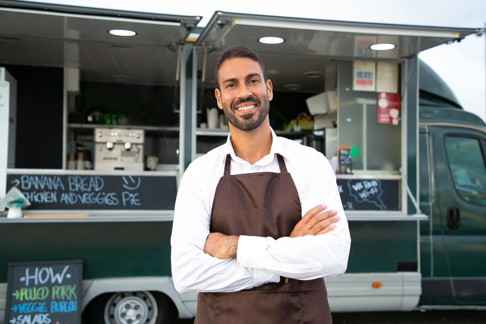 Small Business Owner, smiling with arms folded standing in front of his food truck