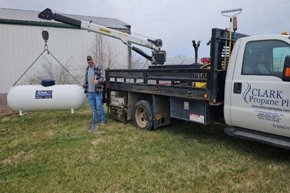 Propane tank being installed by skilled technician with crane-equipped service truck on a farm, emphasizing professional propane services.