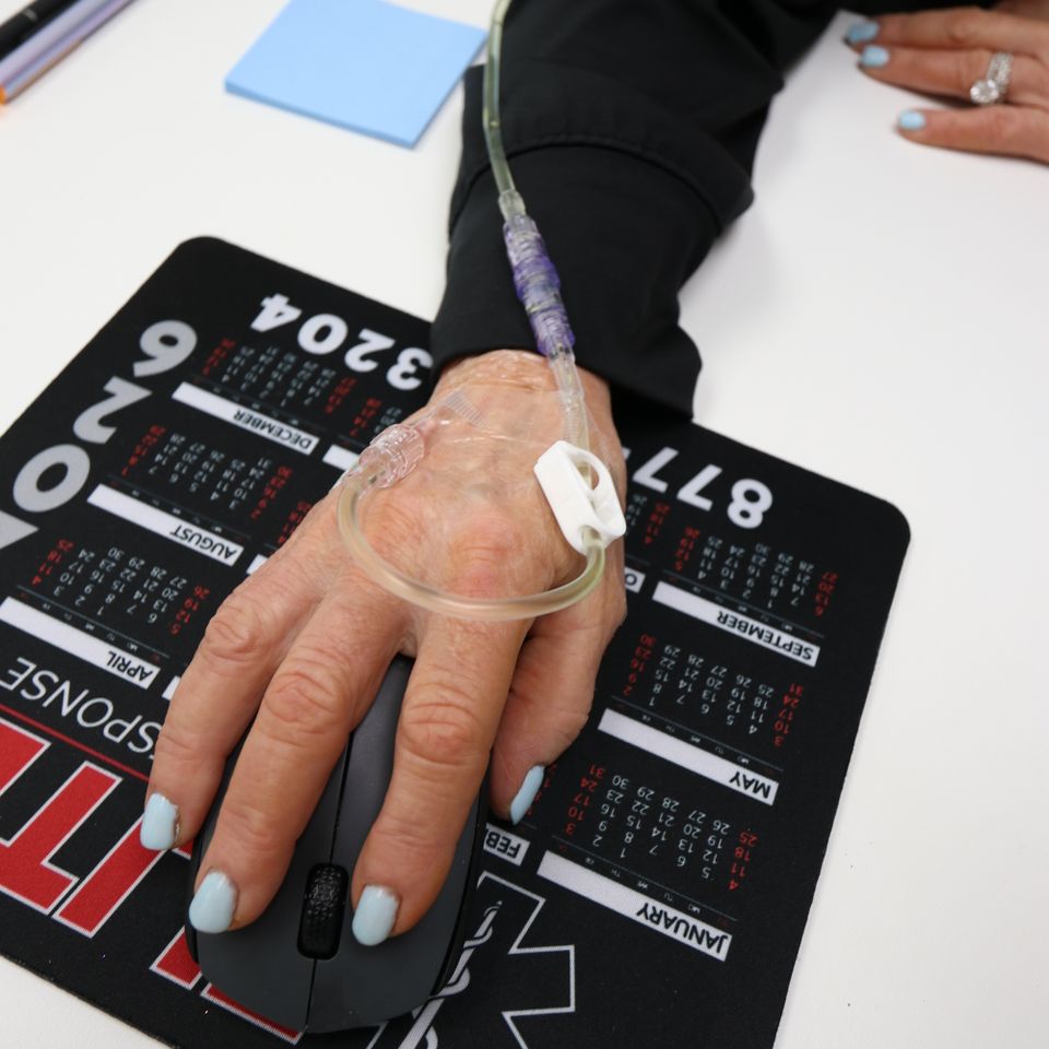 Close up of a hand with an IV catheter secured while using a computer mouse during vitamin drip therapy