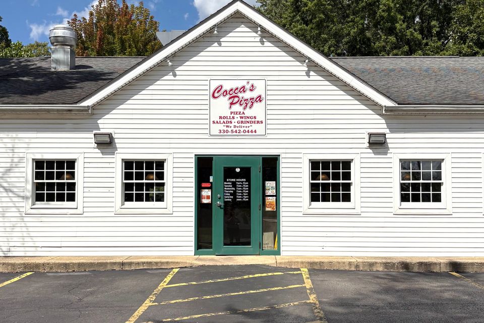 Cocca’s Pizza New Middletown, Ohio location featuring a white-sided building, green entrance doors, and a centered Cocca’s Pizza sign above the entrance.