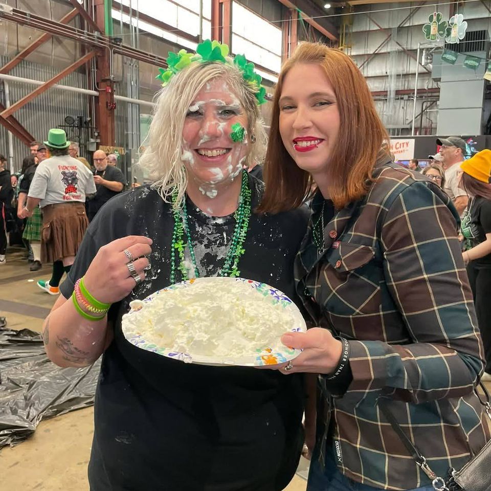 Two women smiling and holding a plate of whipped cream during a St. Patrick’s Day celebration.