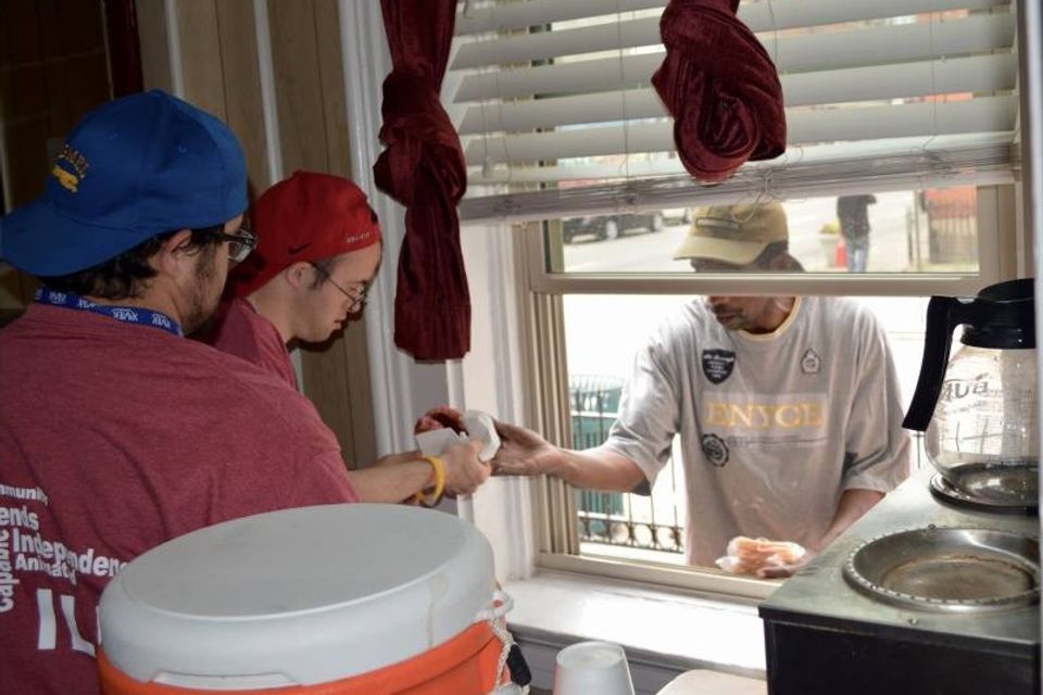 “Volunteers handing food to a man through a service window at the Catholic Worker House.”