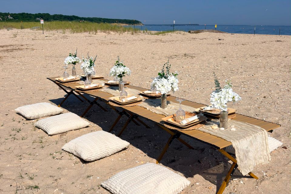 Beach picnic setup with floor cushions and white florals arranged on the sand in the Hamptons