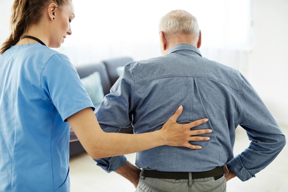 Caregiver supporting senior man with back pain during in home senior care on Long Island NY