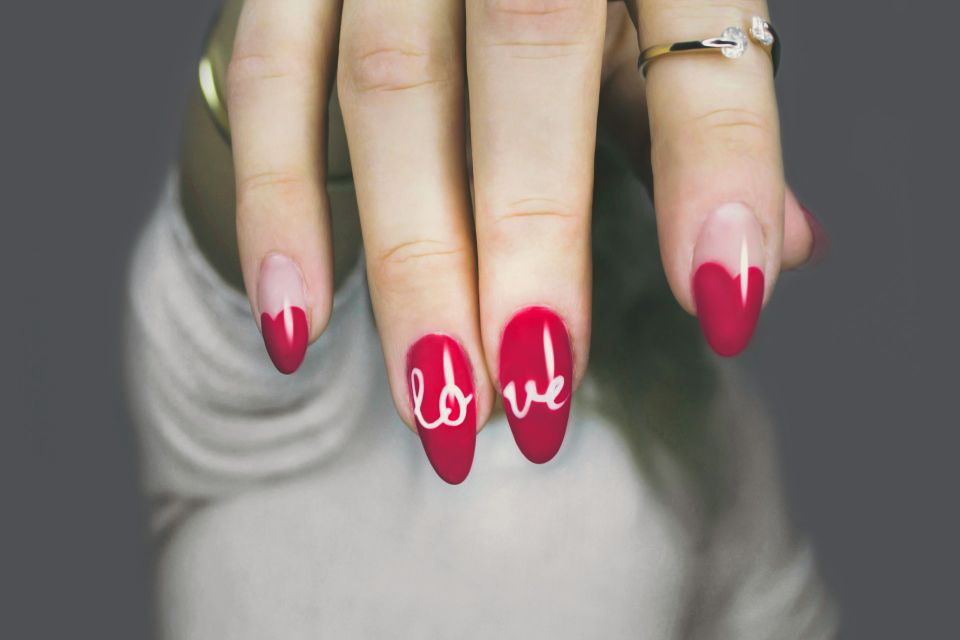 A woman with red nails with the word "love" painted on them after her gel nail service