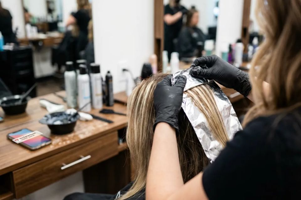 Professional hair stylist applying foil highlights and balayage technique at a local beauty salon