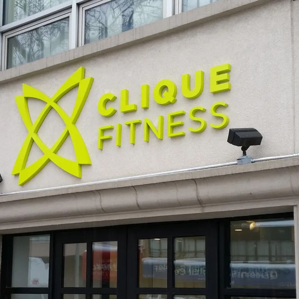 Lime green dimensional letters and a matching logo mounted on a limestone storefront above a glass entrance