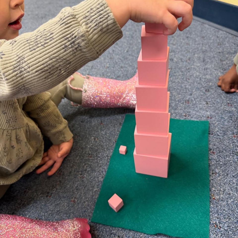 Toddler stacking the Montessori pink tower cubes during a sensorial building activity in Palmdale CA