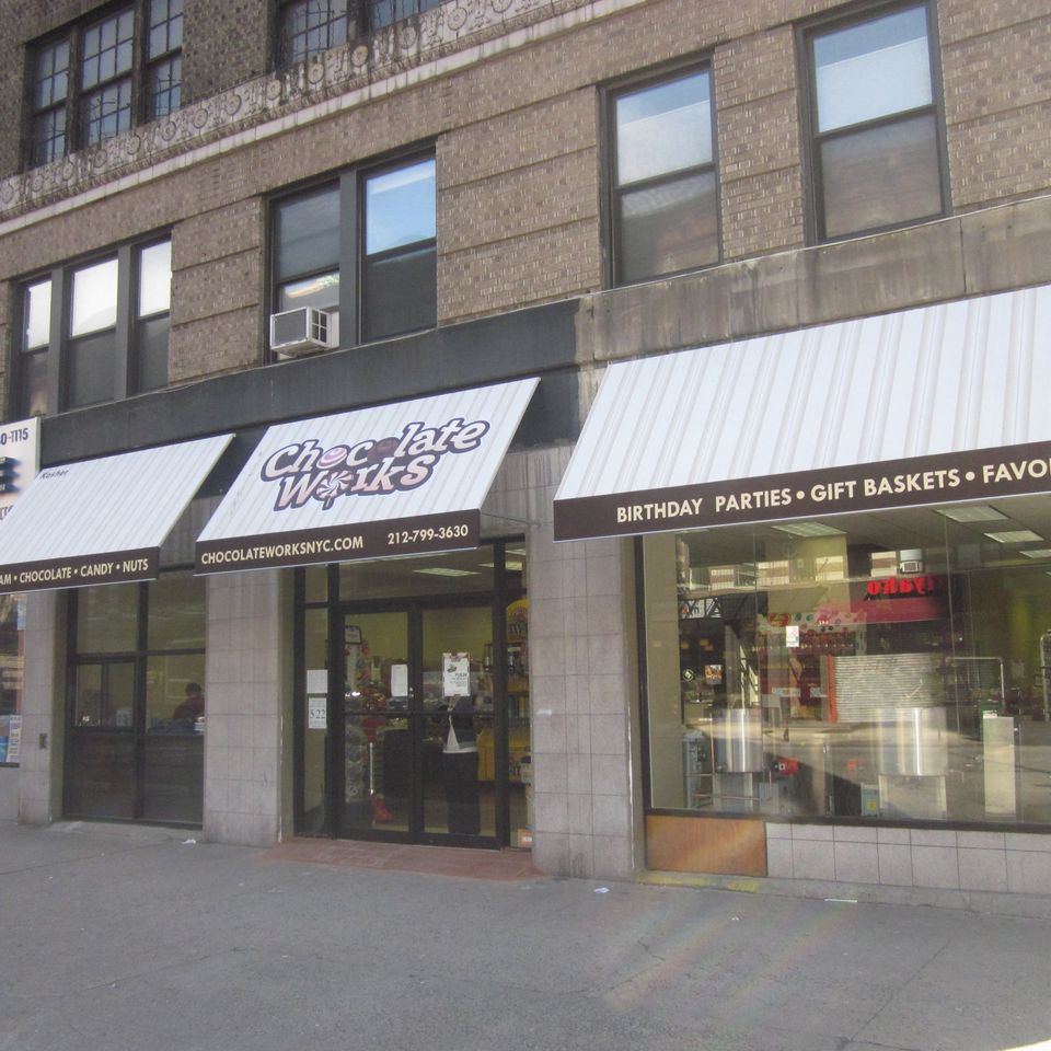 Row of cream storefront awnings with printed lettering across three adjoining retail bays on a New York City building