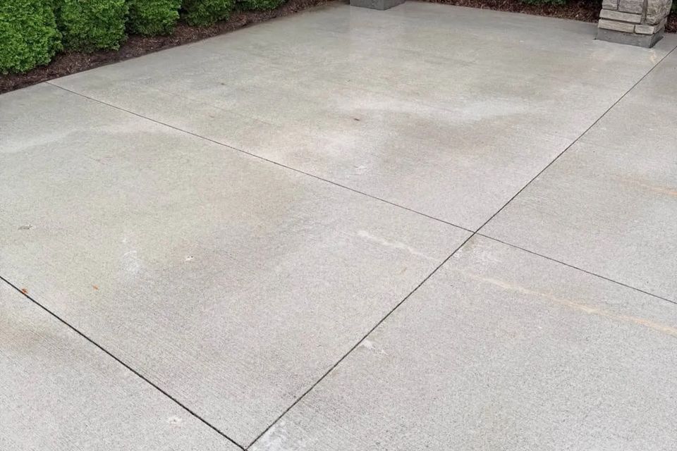 After concrete cleaning, bright stain-free patio with stone pillars and cedar hedge in Tillsonburg Ontario