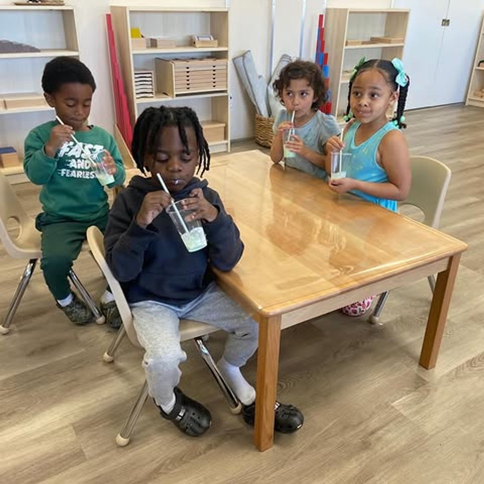 Preschoolers seated at a wooden classroom table sharing smoothies during daycare snack time in Palmdale CA