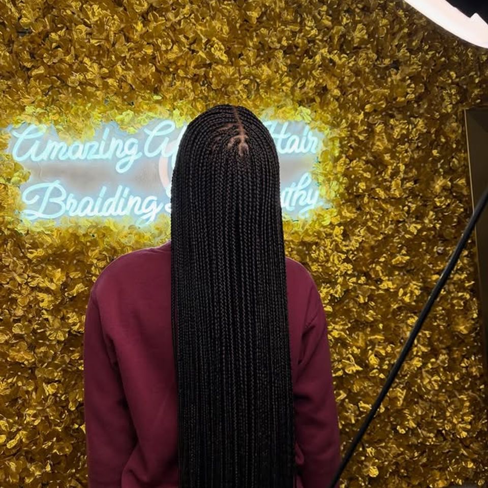 Long waist length knotless braids styled in front of the salon neon sign in Los Angeles CA