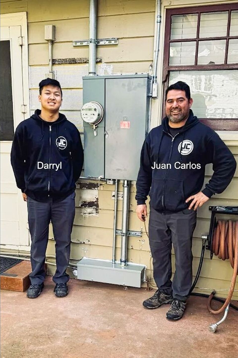 Owners Darryl and Juan Carlos of JC Electrical LLC standing in front of a newly installed residential electrical meter and main service panel.