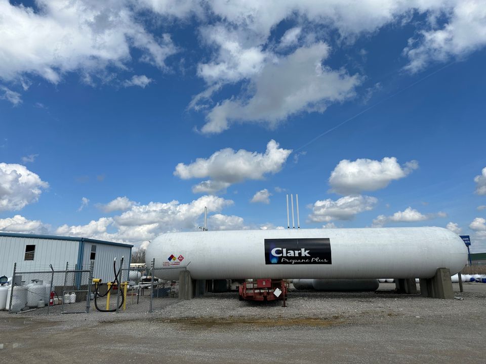 Clark Propane Plus large propane storage tank on a gravel lot with a clear blue sky and scattered clouds overhead.