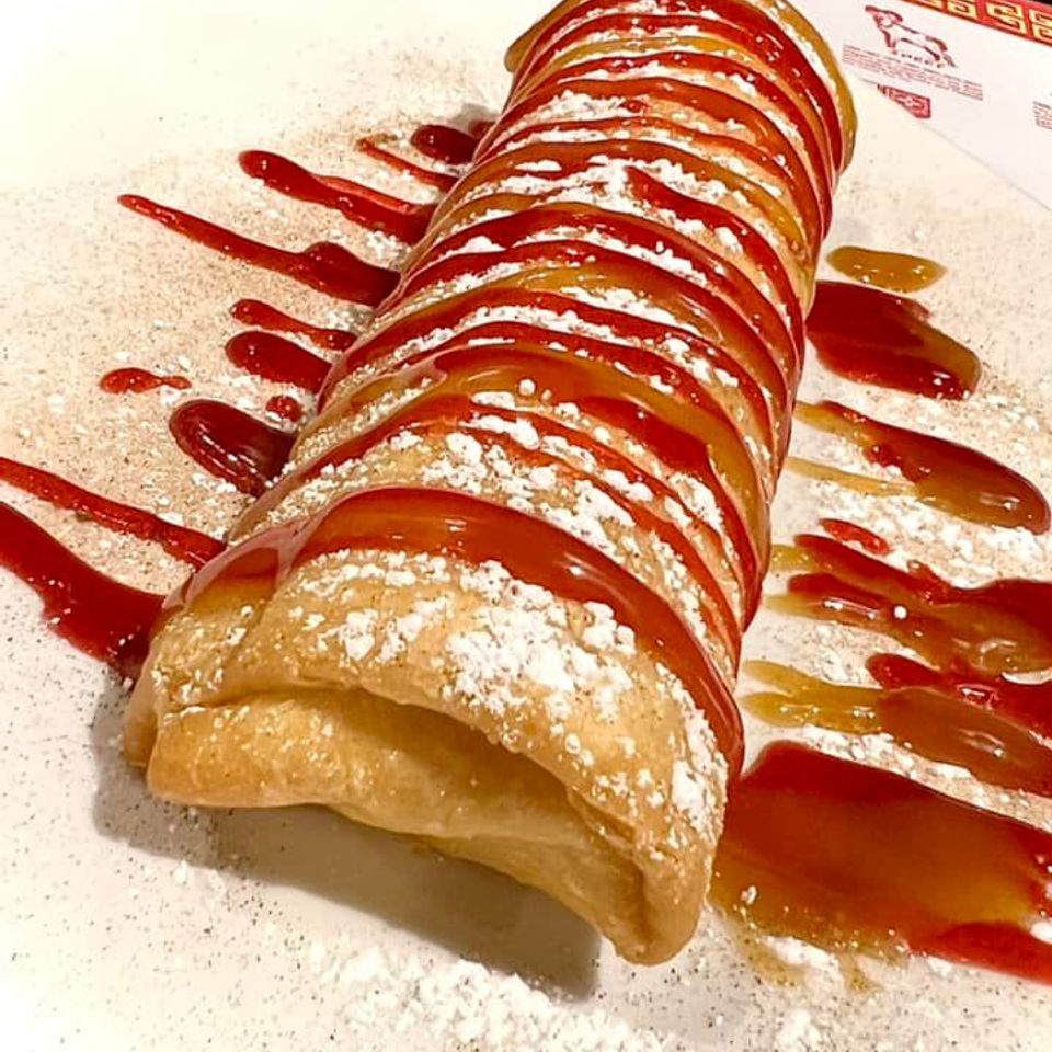 Crispy dessert topped with powdered sugar and drizzled with sweet sauces on a white plate.
