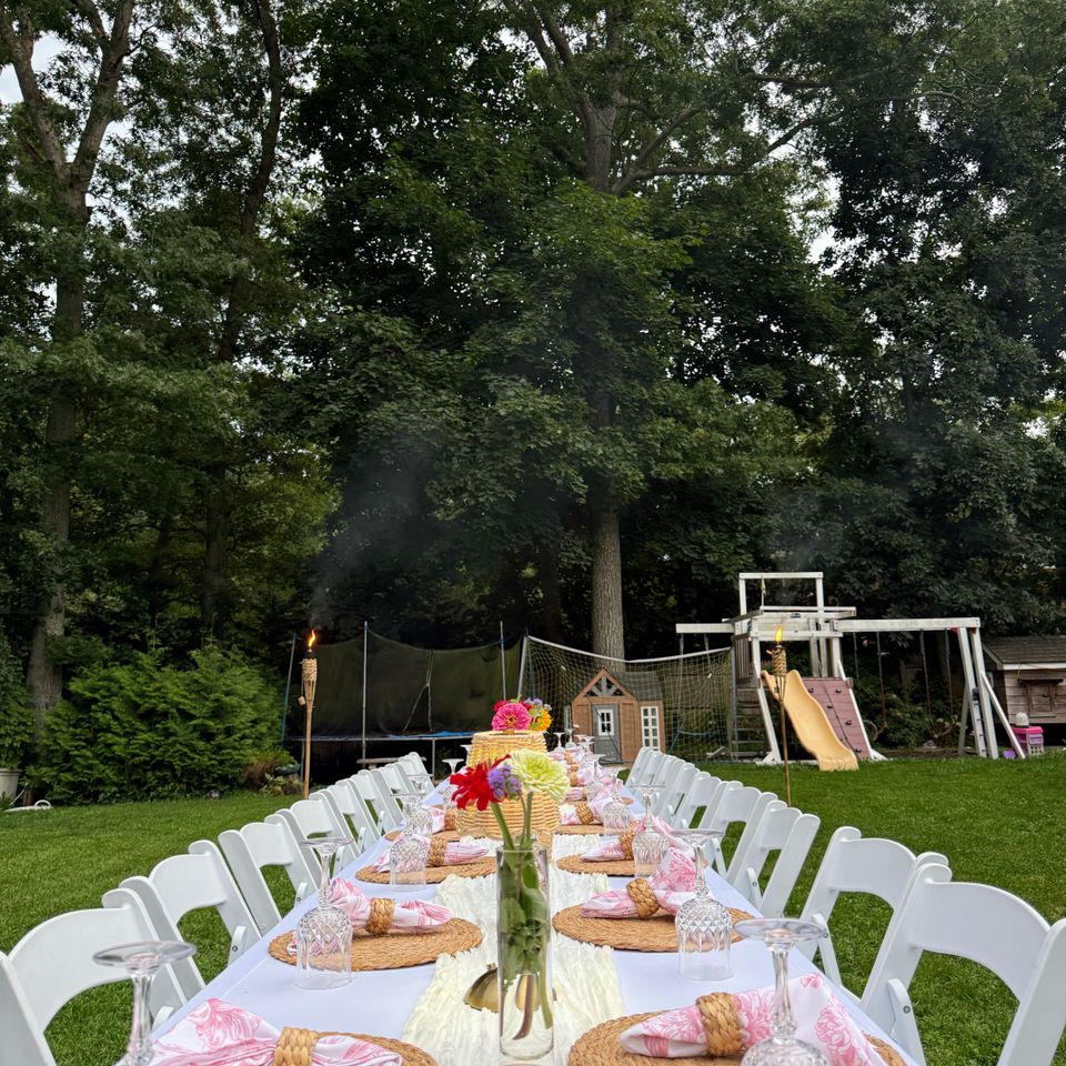 Long backyard banquet table with pink napkins, zinnia centerpiece, and tiki torches in the Hamptons NY