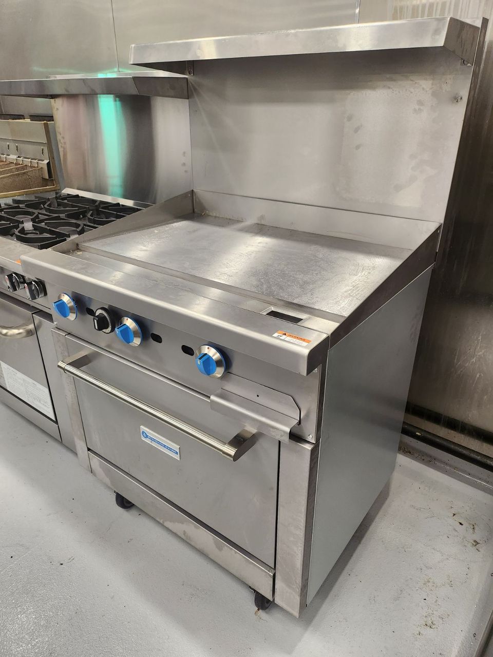 commercial restaurant kitchen flat top grill flat top griddle with oven next to a 6 burner range stove
