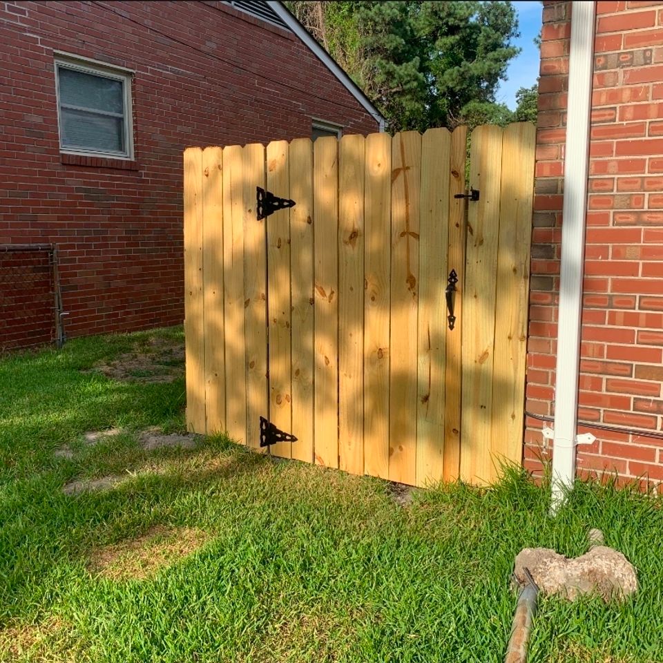 Wood privacy gate with decorative black hinges and latch beside brick home in Virginia Beach VA