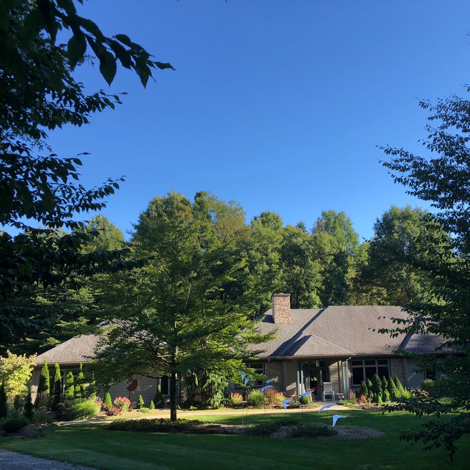 Single-story custom home surrounded by trees, landscaped gardens, and a spacious front yard.