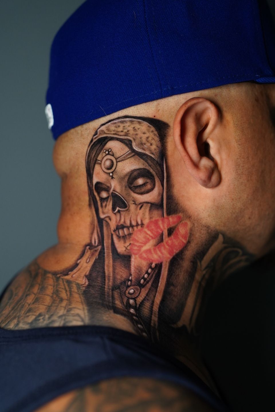 Image of a skeleton tattoo dressed up like a princess and located on the clients neck extending to about the middle of his ear, the tattoo is in black and grey except for a pair of red lips superimposed over the main tattoo.