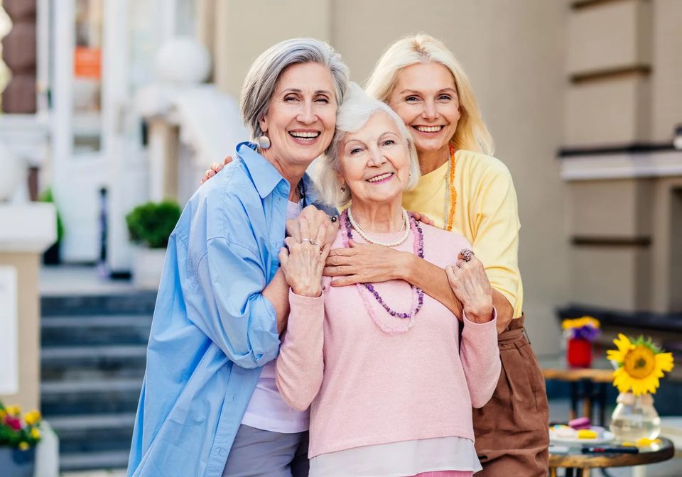 Three senior women smiling together outdoors enjoying senior companion care in Long Island NY