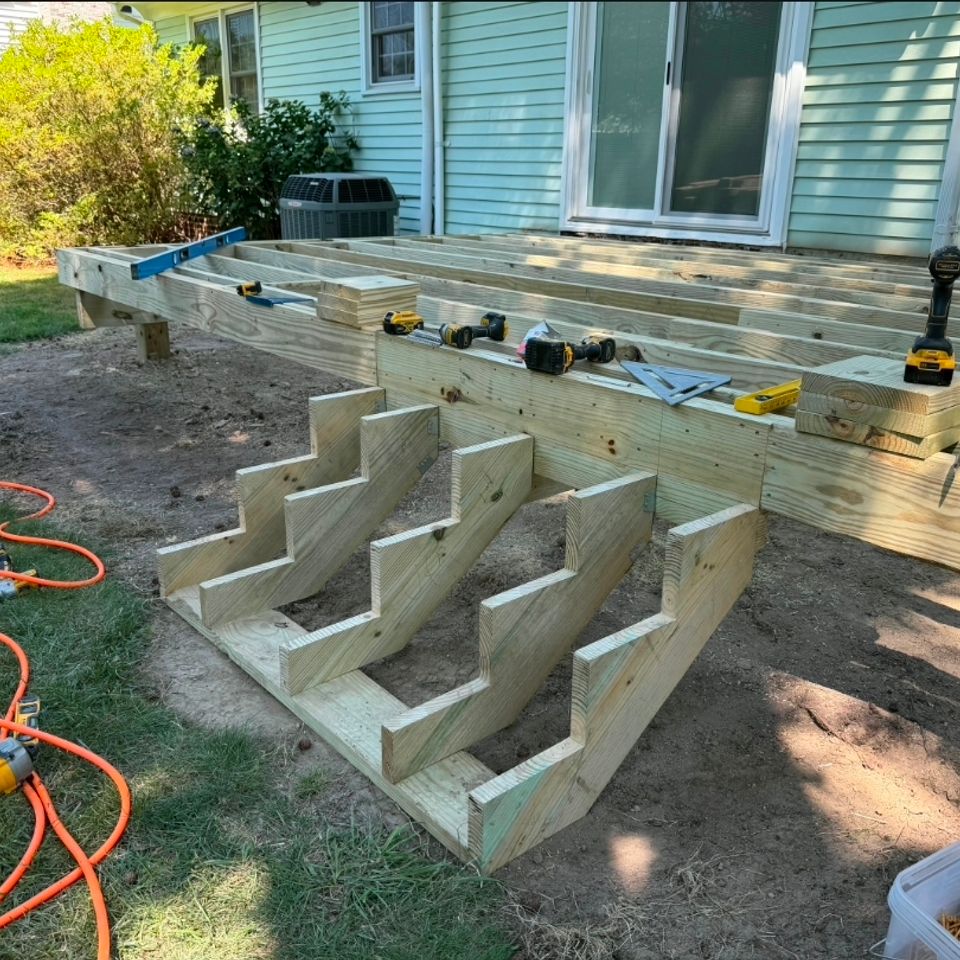 New deck framing with stair stringers under construction behind green home in Virginia Beach VA