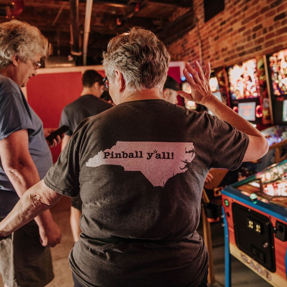 Lady with shirt with the state of North Carolina on the back with words in the middle that read "Pinball y'all"