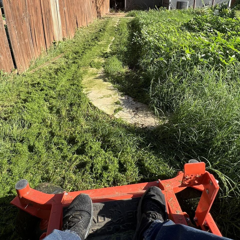 Mowin N Goin stand-on mower cutting an overgrown Lubbock backyard