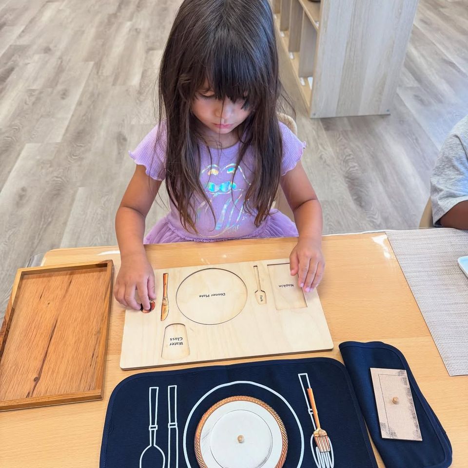 Preschool girl arranging a wooden table setting board during Montessori practical life work in Palmdale CA