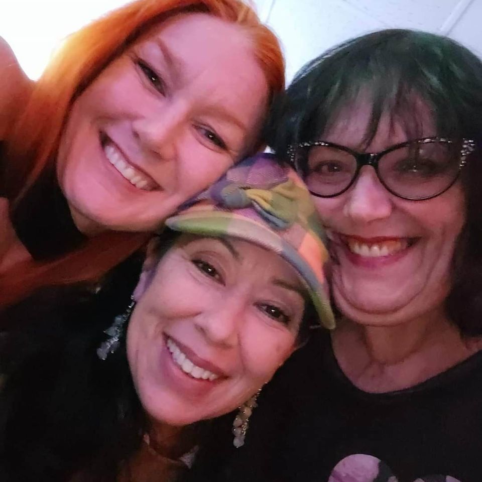 Three women smiling closely together for a group selfie at a social gathering.
