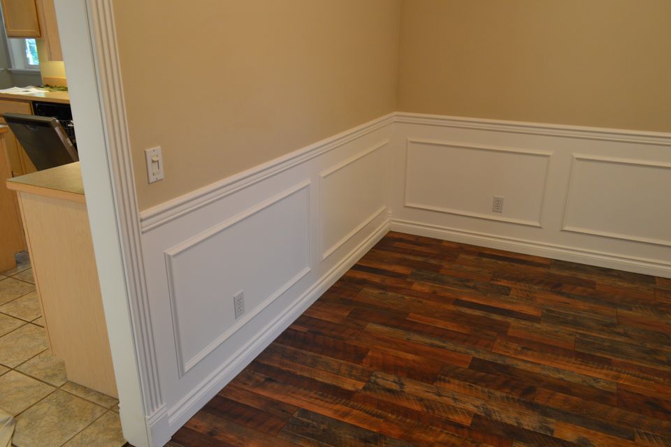 Raised panel wainscoting and white chair rail above reclaimed hardwood flooring in a custom home