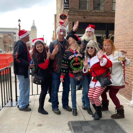 Group of attendees in festive Christmas outfits posing together outside during a holiday event.