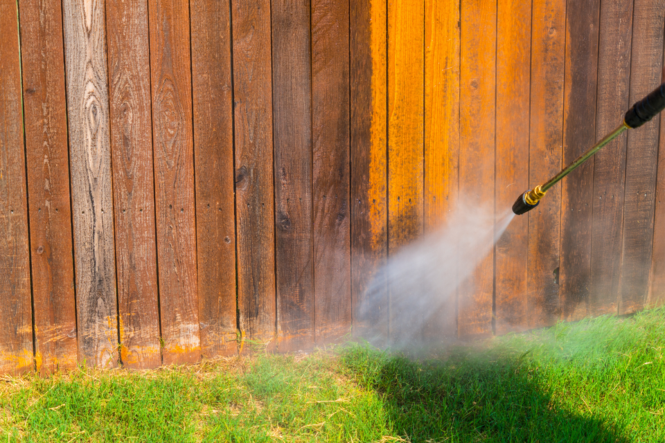 Pressure washing a wooden fence to remove dirt, stains, and buildup.