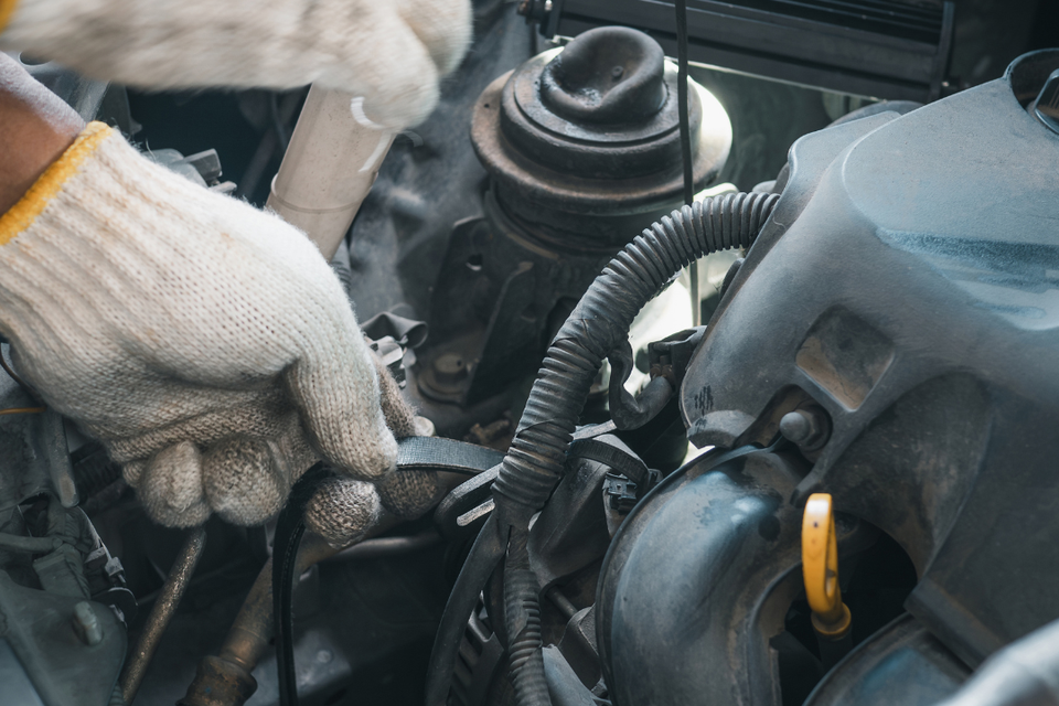 Technician performing engine repair and maintenance under the hood of a vehicle.