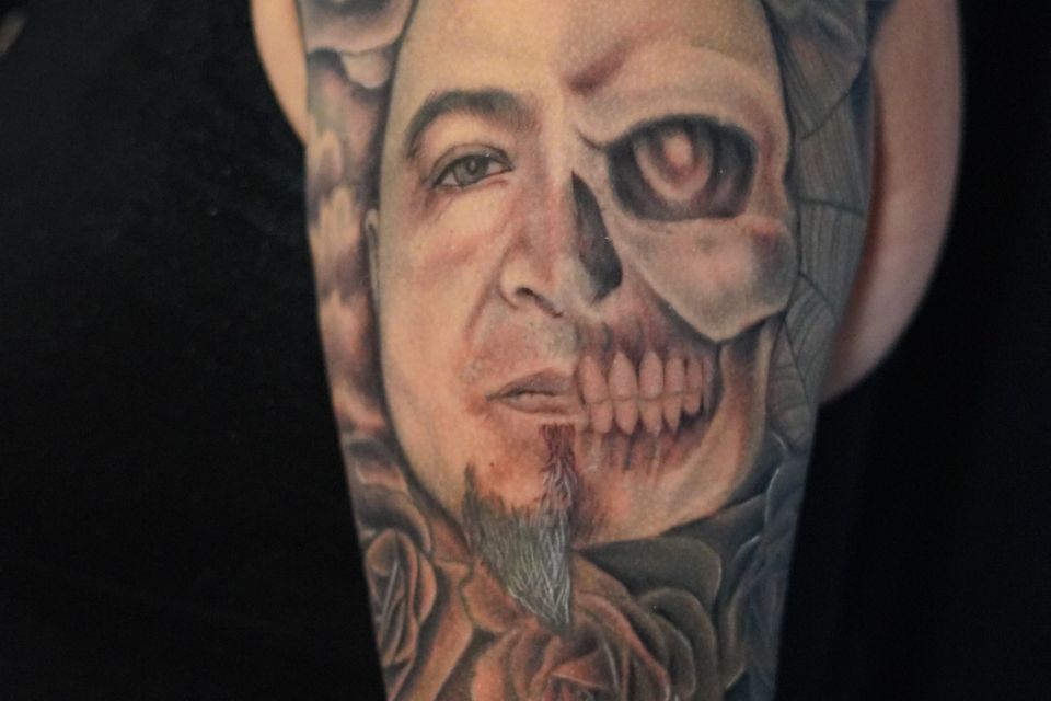 Image of a tattoo showing a half face and half skeleton in great detail surrounded by incredibly detailed flowers