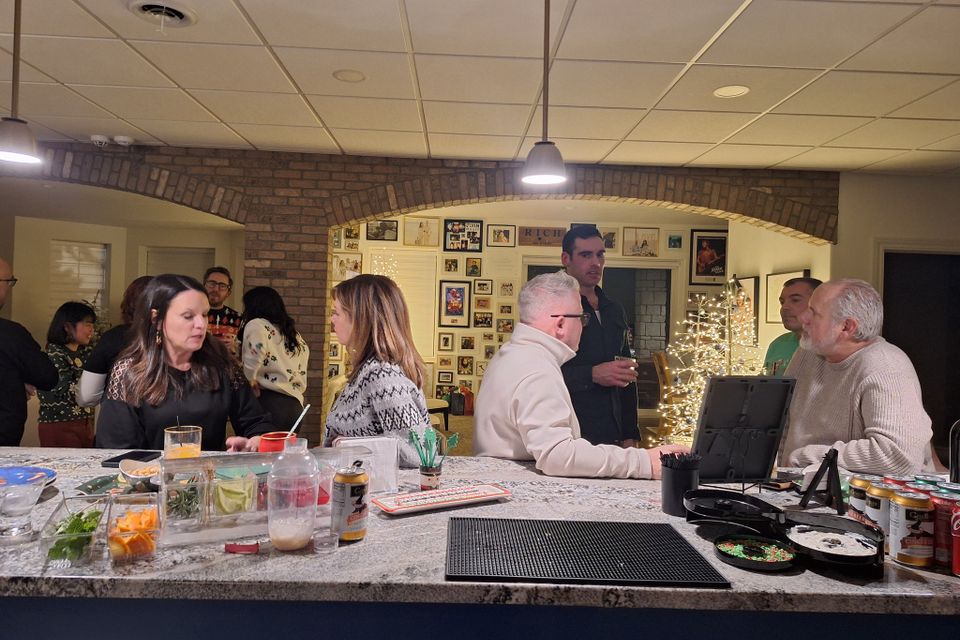People gathered around a bar area with drinks and garnishes at a holiday party