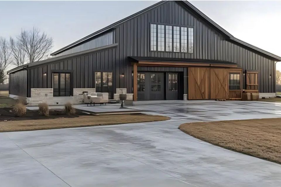 Black metal barndominium with vertical siding, sliding barn door, and wide concrete driveway
