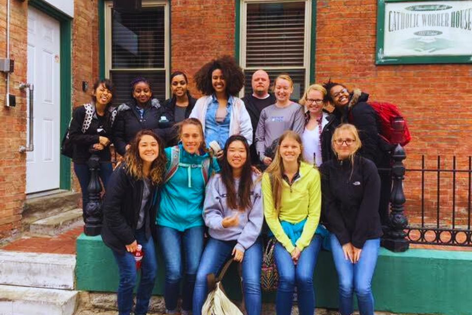 “Group of volunteers smiling together in front of the Catholic Worker House building.”