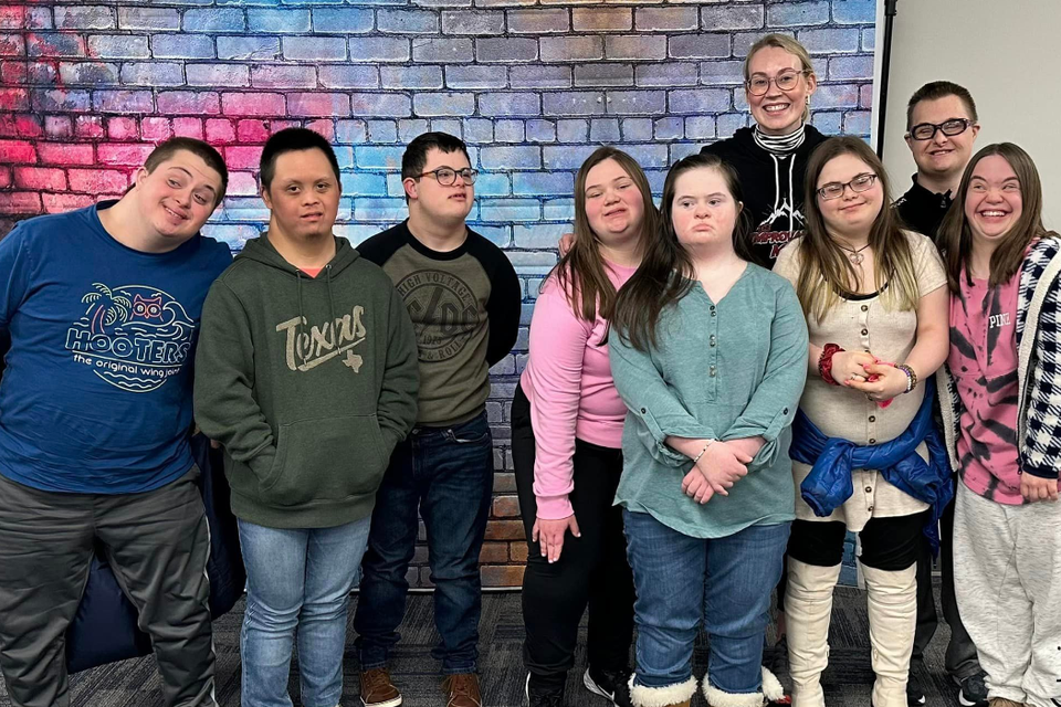Participants with Down syndrome and their instructor posing together in front of a colorful brick backdrop during an improv class.