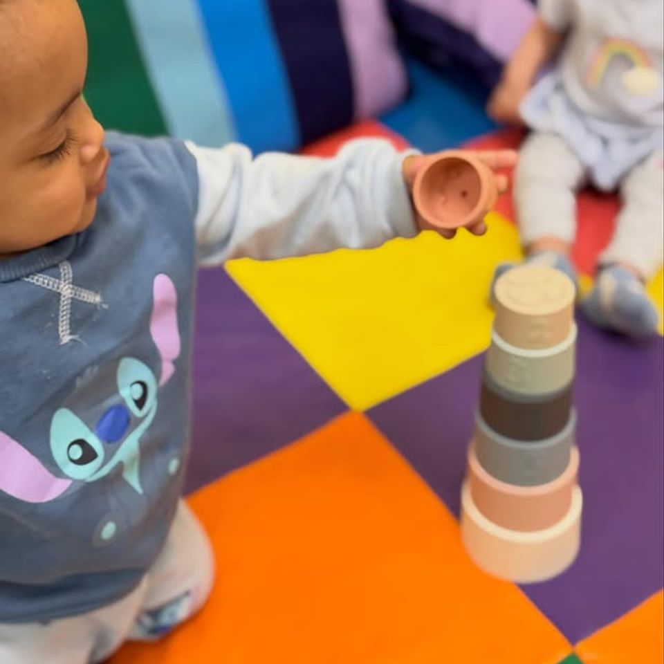 Toddler stacking nesting cups on a colorful play mat during infant daycare activities in Palmdale CA
